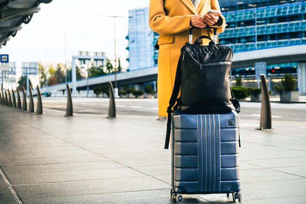 woman traveler in coat with handbag and suitcase orders taxi midas travel management travel managers should start travel planning now before the autumn rush
