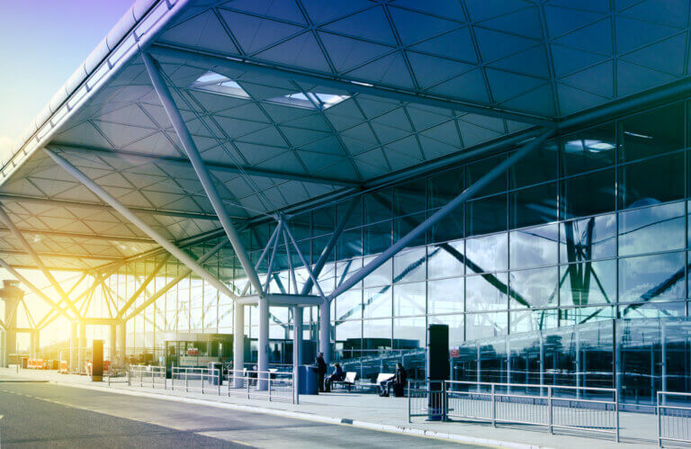modern airport terminal exterior with glass walls and exposed steel framework in morning sunlight