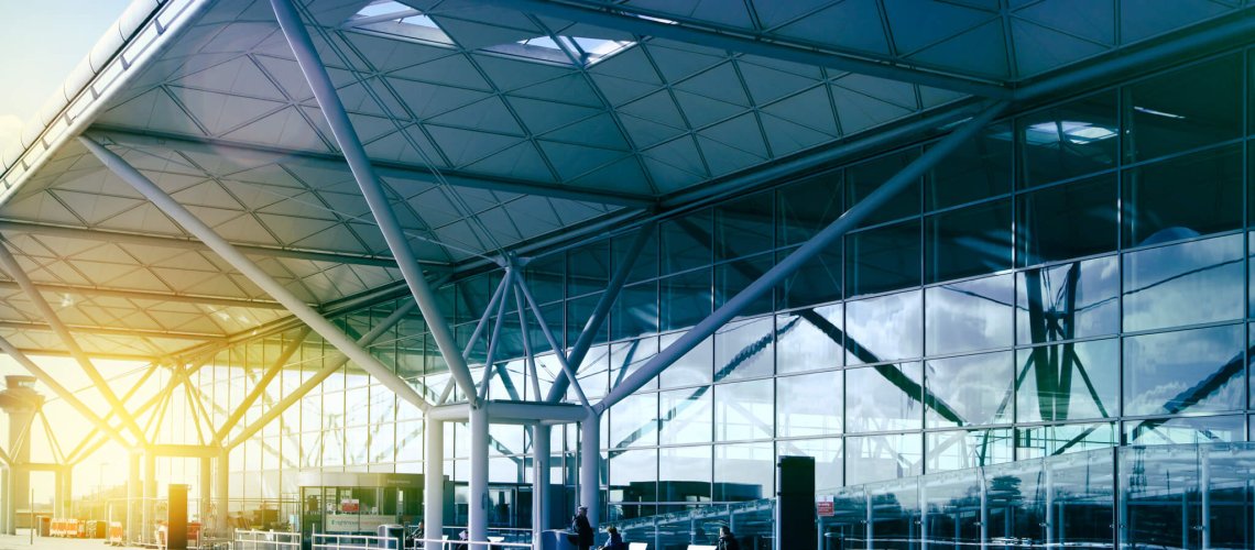 Modern airport terminal exterior with glass walls and exposed steel framework in morning sunlight.